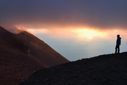 Italie, Sicile, iles Eoliennes, classées Patrimoine Mondial de l'UNESCO, ile de Stromboli, randonneur observant les fumerolles d'une éruption sur les pentes du volcan actif au coucher de soleil
