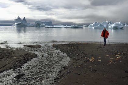 Greenland, west coast, Disko Island, Qeqertarsuaq village bay, hiker on the beach and icebergs in the background