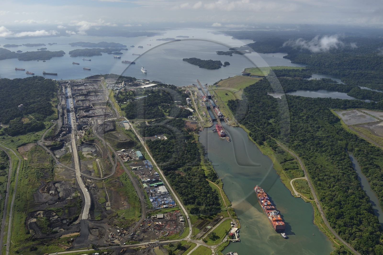 Panama, Colon province, Panama Canal, Panamax cargo passing the Gatun locks, the construction of the new locks on the left and the Gatun Lake in the background (aerial view)