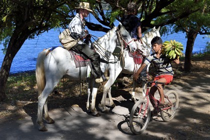Nicaragua, Ile d'Ometepe sur le lac Nicaragua, cavaliers en randonnée en bordure du lac et jeune cycliste transportant un régime de banane