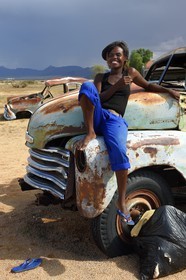 Namibie, région de Khomas, désert du Namib à l'Est du parc national Namib Naukluft, station essence de Solitaire, Gloria une jeune routarde namibienne qui fait la route assise sur la carcasse d'un pick-up Chevrolet