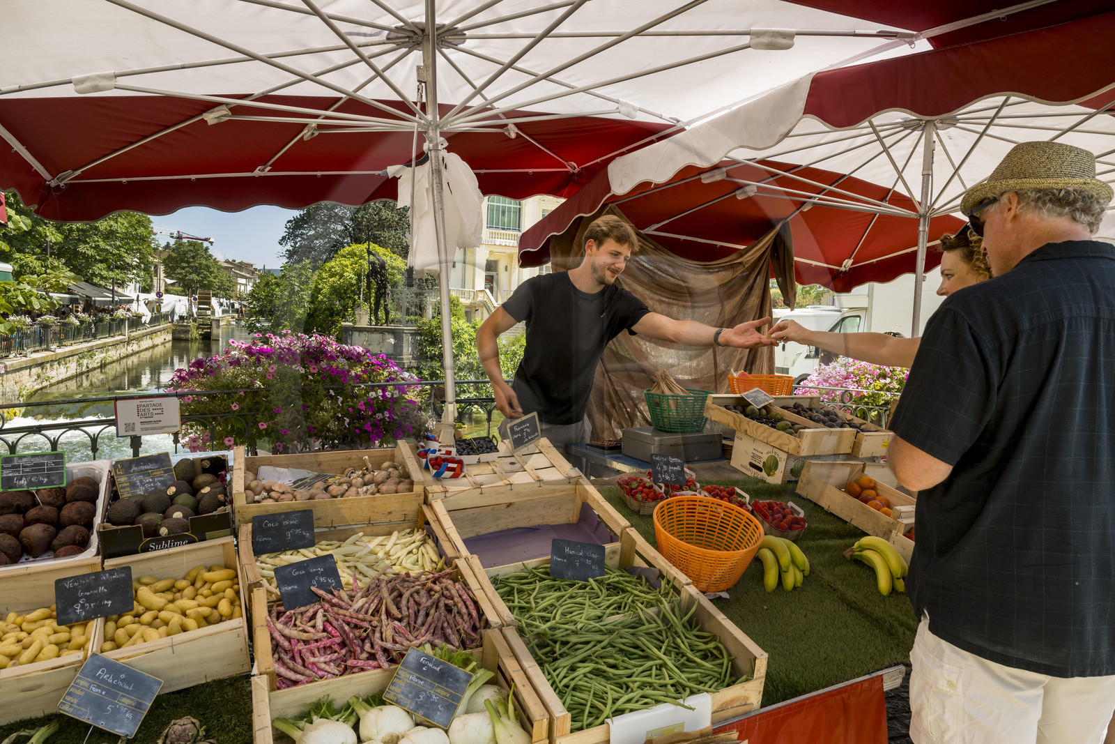 France, Vaucluse (84), L'Isle-sur-la-Sorgue, jour de marché, Justin sert une cliente de son étal de fruits et légumes sur un pont de la Sorgue