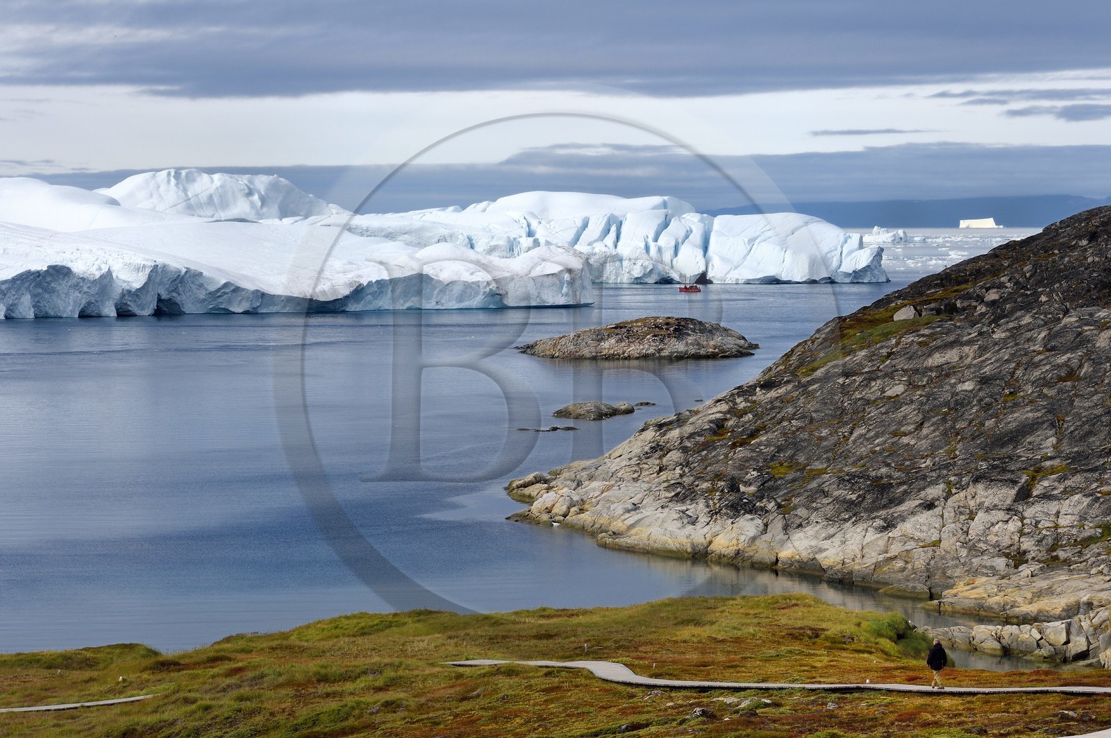 Greenland, west coast, Disko Bay, Ilulissat, icefjord listed as World heritage by UNESCO that is the mouth of the Sermeq Kujalleq Glacier (Jakobshavn Glacier), hiking on the wooden walkway going to the Sermermiut site and fishing boat at the foot of icebergs