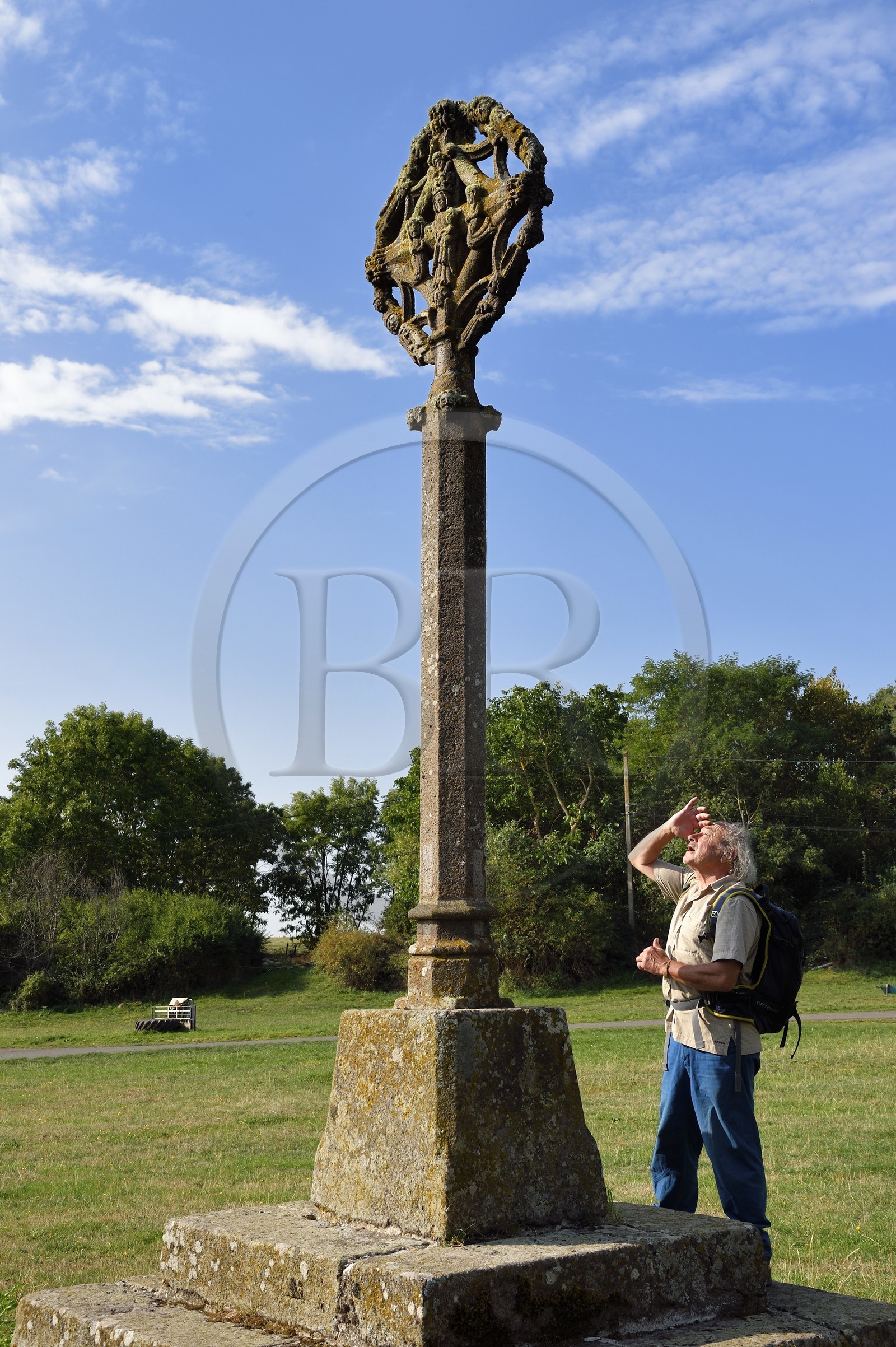 France, Cantal, Parc Naturel Régional des Volcans d'Auvergne (regional nature park of Auvergne volcanoes), hiker on the Way of St. James to Santiago de Compostela by Via Arverna, Chalinargues, the 15th century granite Cross of Mons, on this side we can see the Virgin surrounded by angels, kneeling people and saints, on the other Christ