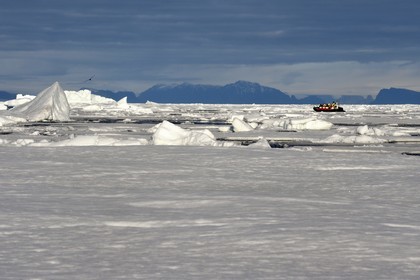 Greenland, North West coast, Smith sound north of Baffin Bay, broken pieces of Arctic sea ice and an exploration PolarCirkel boat (zodiac) of the MS Fram cruse ship from Hurtigruten, giant iceberg in the background towards the Canadian coast of Ellesmere Island