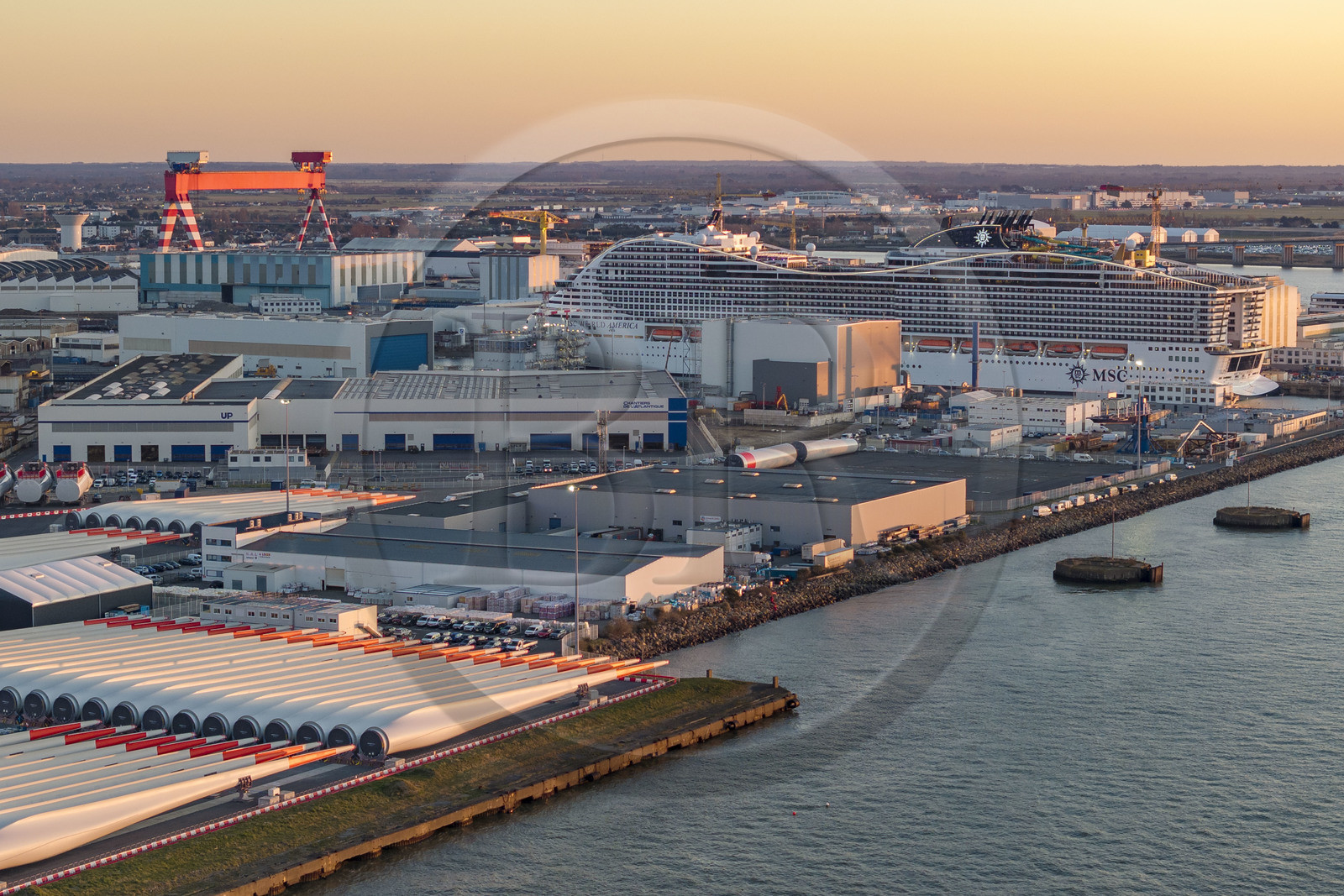 France, Loire-Atlantique (44), Saint-Nazaire, les tours d'éoliennes et les pales sont stockées avant embarquement, le paquebot de 333m MSC World America construit par les Chantiers de l'Atlantique en arrière plan (vue aérienne)