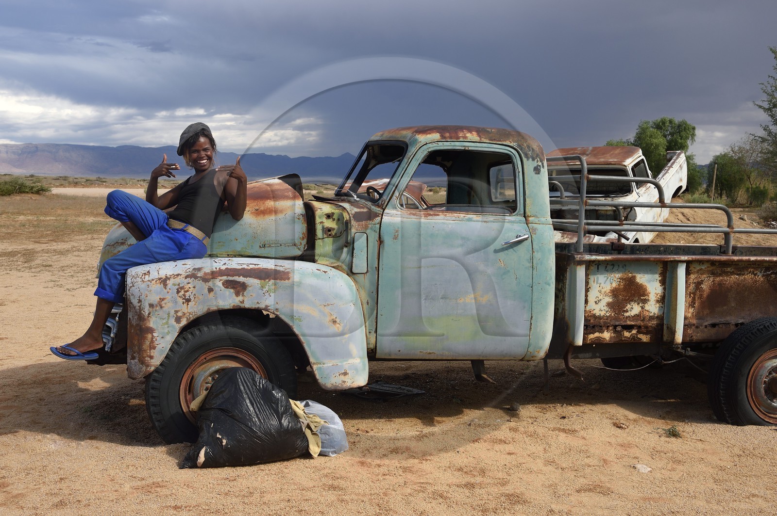 Namibie, région de Khomas, désert du Namib à l'Est du parc national Namib Naukluft, station essence de Solitaire, Gloria une jeune routarde namibienne qui fait la route assise sur la carcasse d'un pick-up Chevrolet