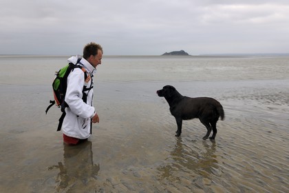 France, Manche, walking discovery of the Bay of Mont Saint Michel, the guide Romain Pilon deep in the sand and Tombelaine island in the background