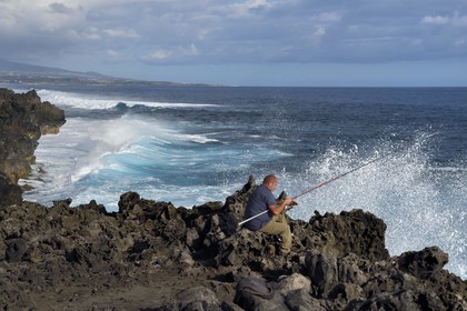 France, Ile de la Reunion, L'Etang Salé les Bains, la côte entre Le Gouffre et l'Etang du Gol, roches noires basaltiques d'origine volcanique tourmentées par l'océan, pêcheur à la ligne