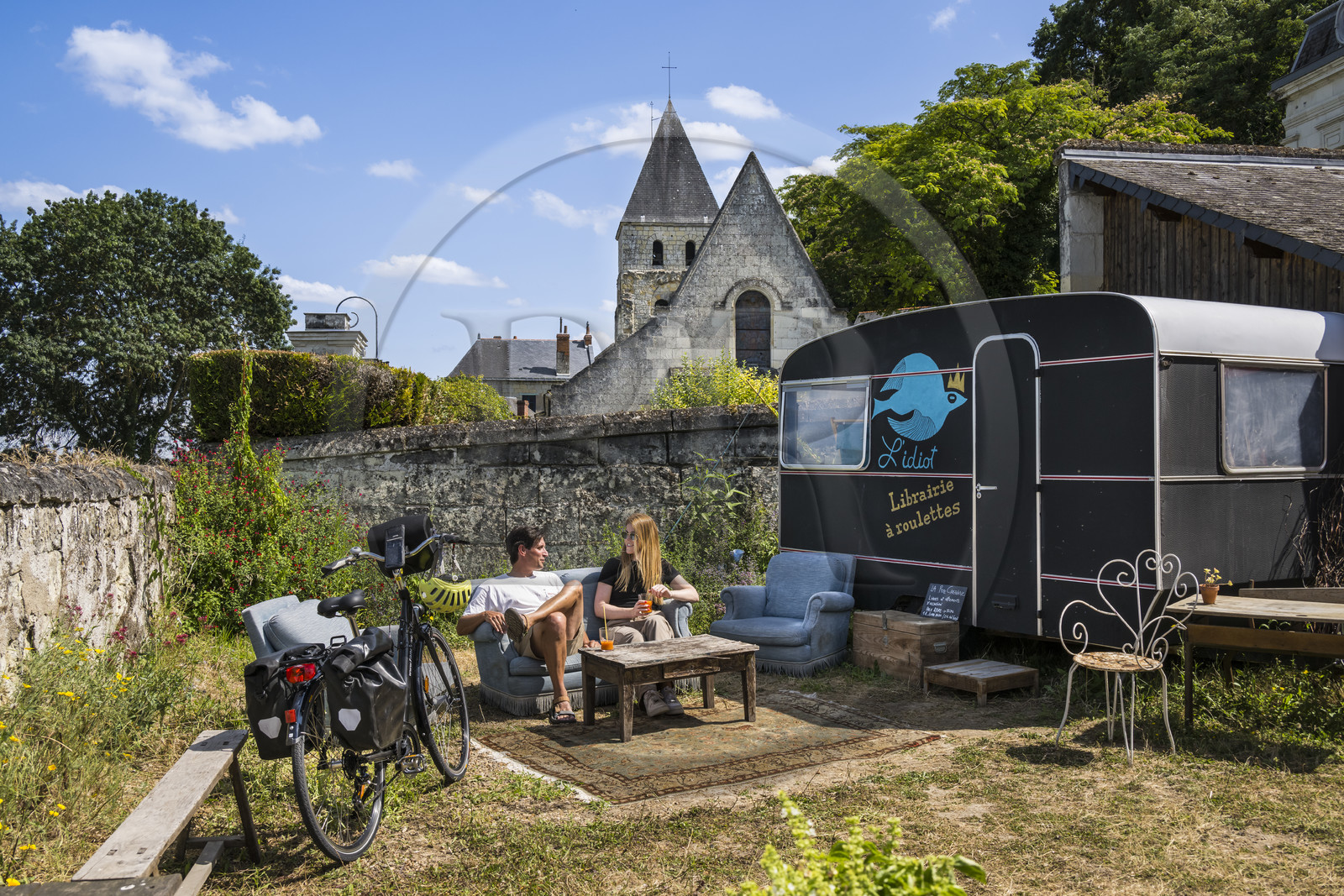 France, Maine-et-Loire (49), vallée de la Loire classée au Patrimoine Mondial par l'UNESCO, Gennes-Val-de-Loire, randonnée à bicyclette sur les berges de la Loire, pause à la librairie-café L'Idiot de l'association Gabare And Co dans l'ancienne école des Filles de Chênehutte, l'église notre dame des tuffeaux en arrière plan