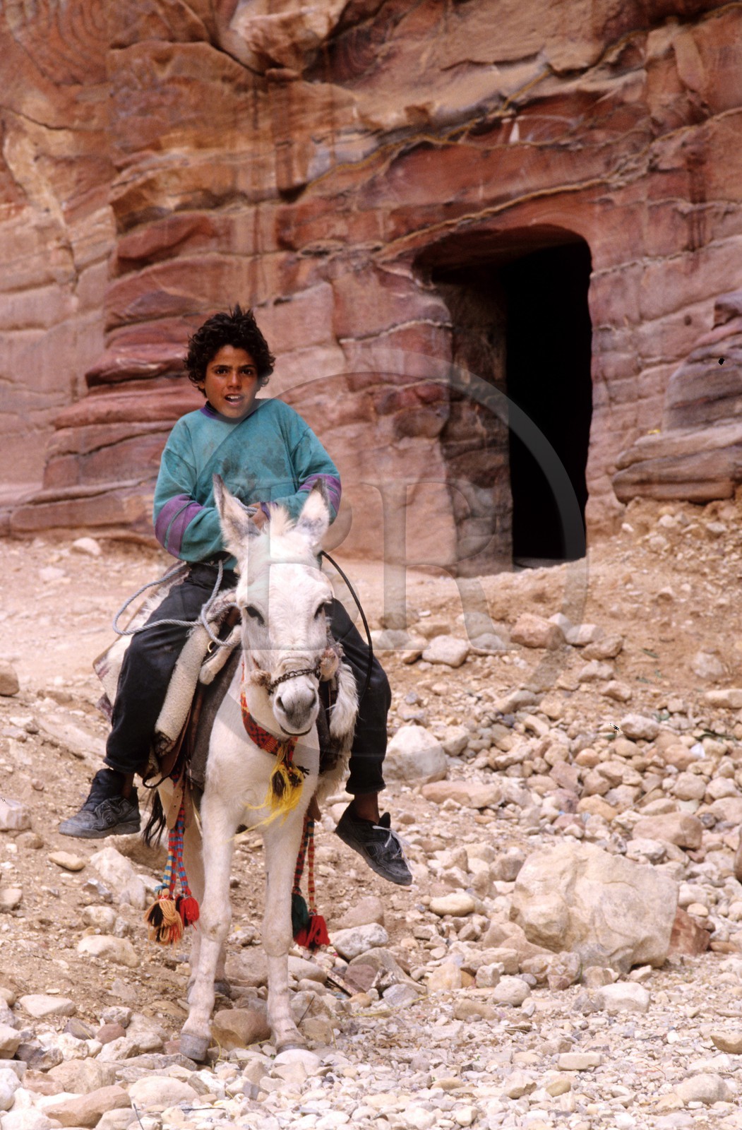 Jordan, Petra, young Bedouin in front of the facade of a grave in the outside Siq