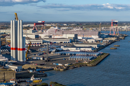 France, Loire-Atlantique (44), Saint-Nazaire, les tours d'éoliennes et les pales sont stockées avant embarquement, le paquebot de 333m MSC World America construit par les Chantiers de l'Atlantique en arrière plan (vue aérienne)