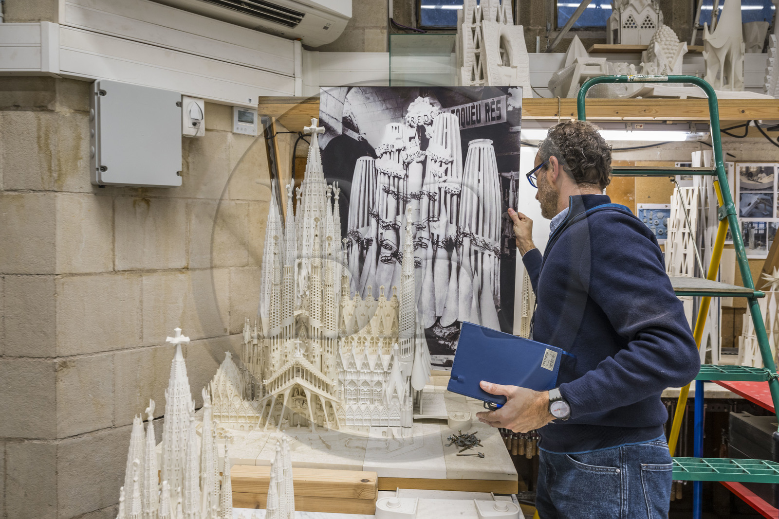 Espagne, Catalogne, Barcelone, quartier de l'Eixample, basilique de la Sagrada Familia de l'architecte du modernisme catalan Antoni Gaudi classée Patrimoine Mondial de l'UNESCO, l'atelier maquettes, l'architecte et coordinateur de l'équipe des artistes et des maquettistes Jeronimo Buxareu Padros présente les prochains travaux à entreprendre, la future facade de la Gloire face à lui et la photo de la maquette originale de Gaudi en arrière plan