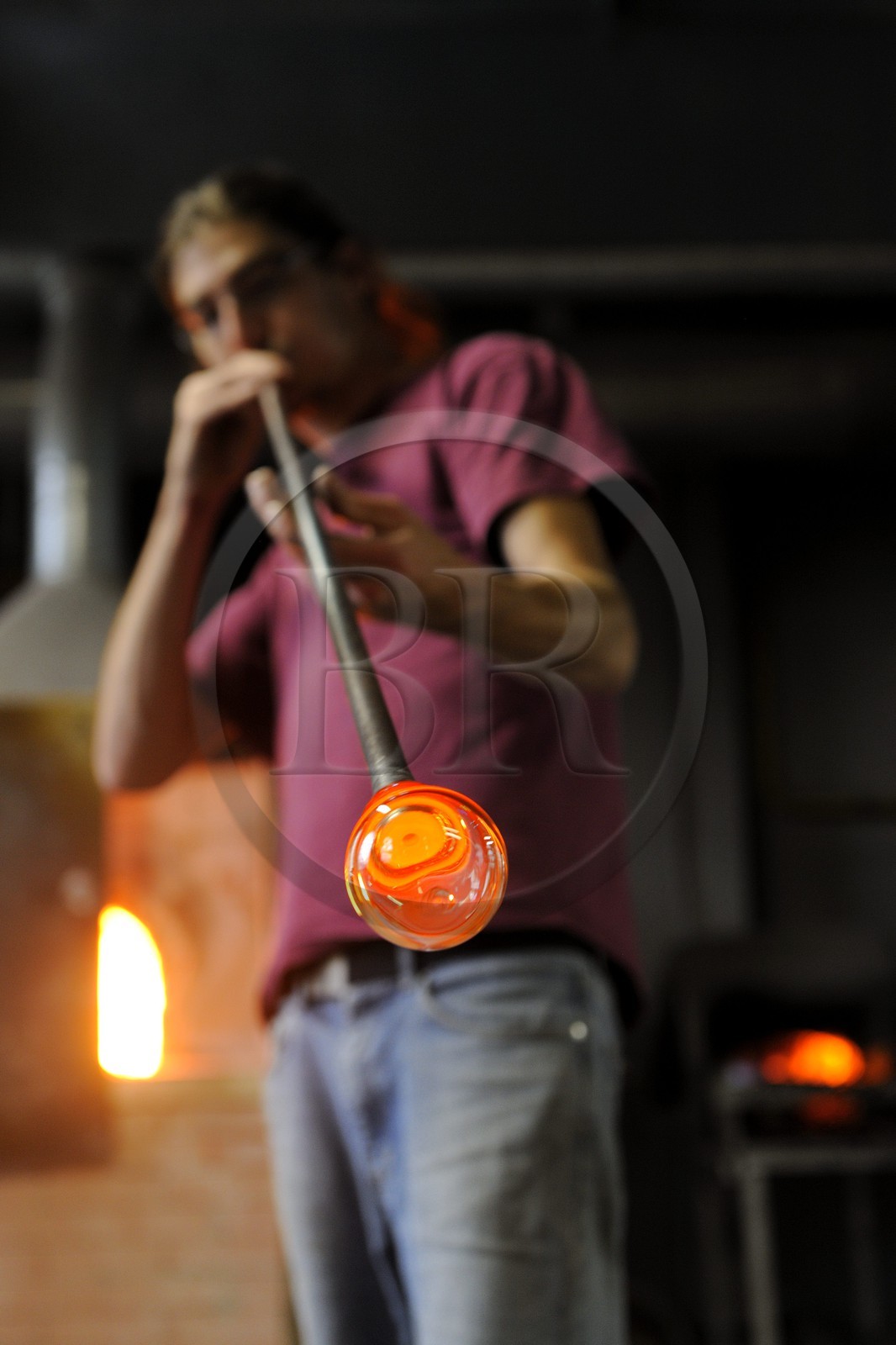 France, Moselle (57), Meisenthal, Thibaut souffleur au Centre international d’Art verrier (CIAV), fabrication d'une boule de Noël en verre. Tout en tournant la canne, il souffle dans la canne