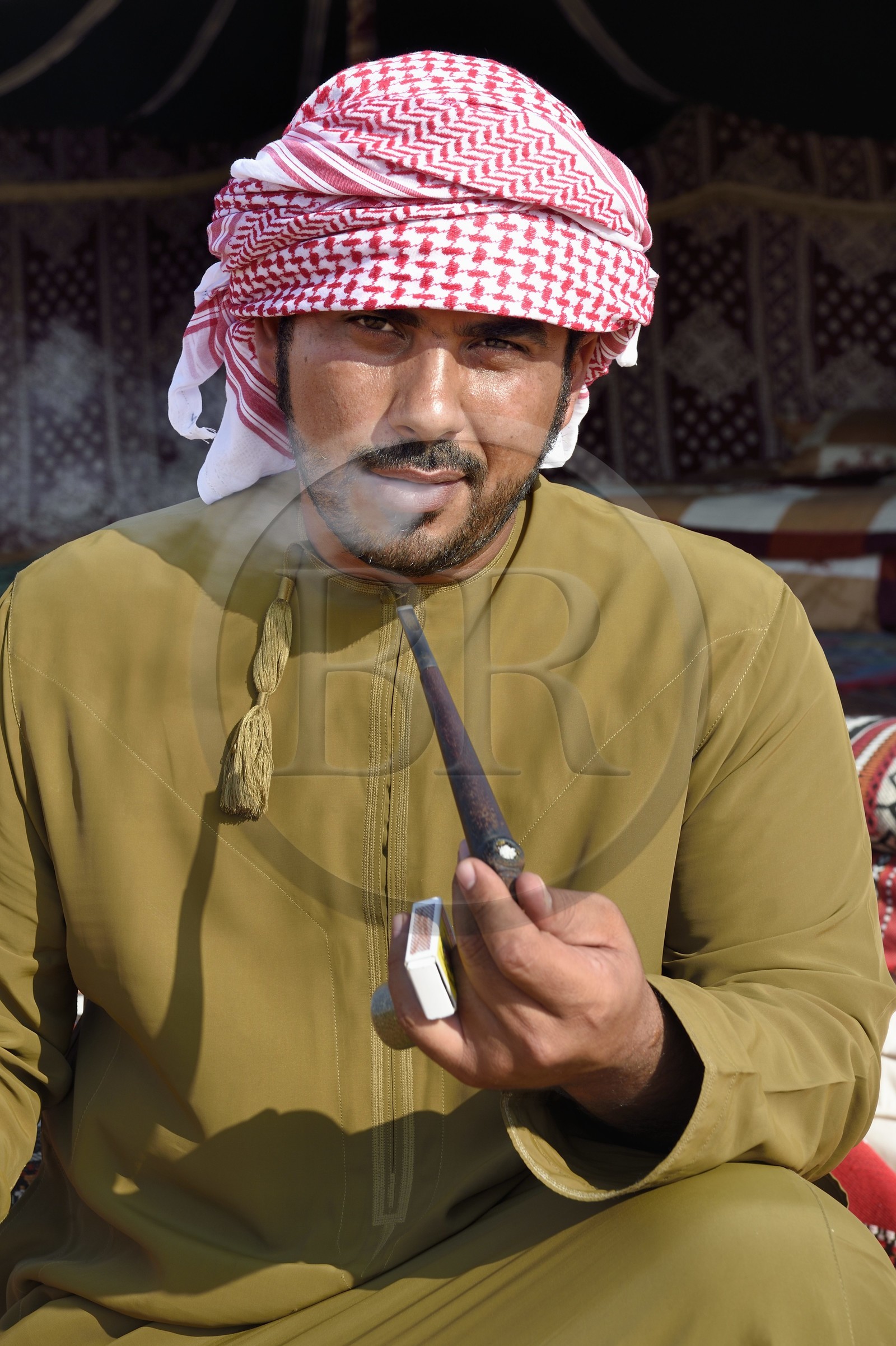 Sultanat d'Oman, gouvernorat de Ash Sharqiyah, désert des Wahiba Sands ou Sharqiya Sands, village bédouin de al-Wasil, Mohamed al-Badri fume la pipe devant sa tente