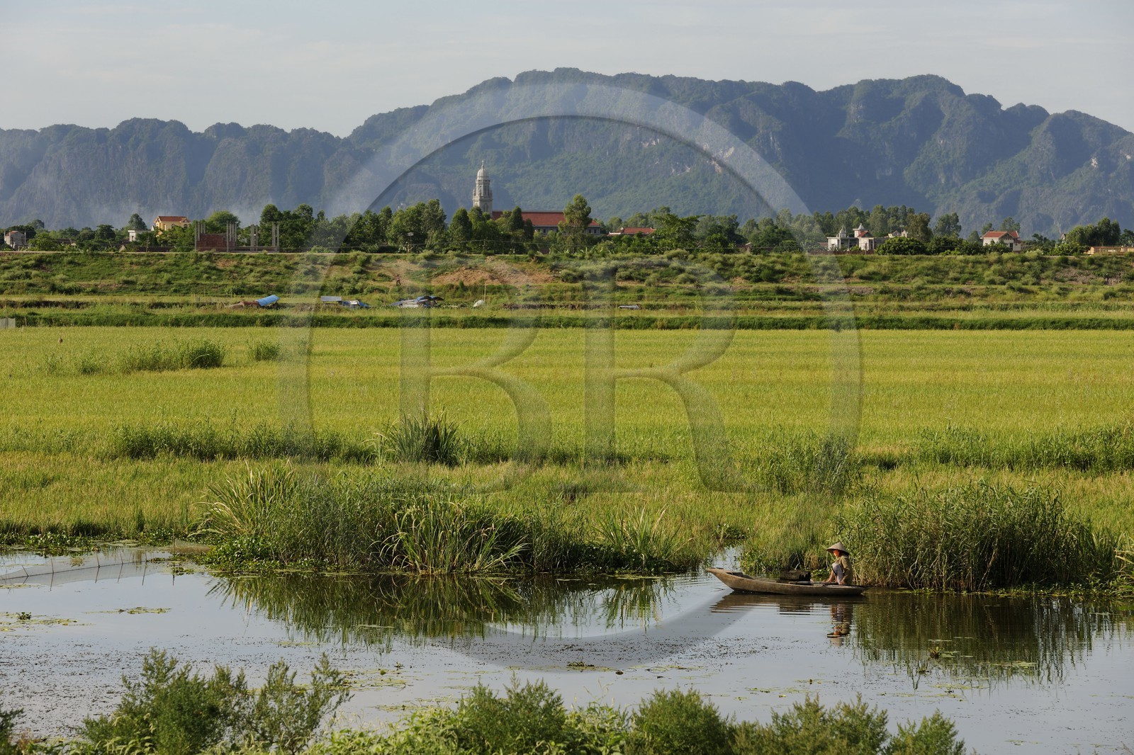 Vietnam, province de Ninh Binh, pêcheur en barque devant un village chrétien