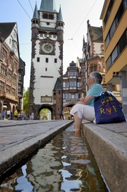 Allemagne, Bade-Wurtemberg, Fribourg en Brisgau, un des Bächle qui sont des petits caniveaux ouverts qui bordent les trottoirs de la vieille ville, Kaiser-Joseph Strasse et la Porte Saint-Martin Martinstor en arrière plan