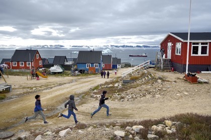 Groenland, cote Nord-Ouest, mer de Baffin, Qaanaaq ou Nouvelle Thule, des enfants inuit courent rejoindre leur maitresse d'école, un iceberg en arrière plan