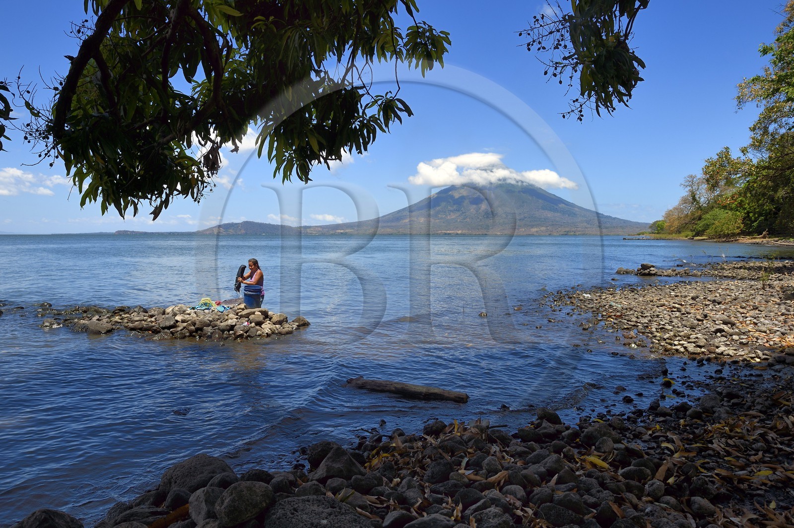 Nicaragua, Ometepe Island in Lake Nicaragua, village of Merida, woman doing her laundry in the lake and the Conception volcano (1610 m) in the background