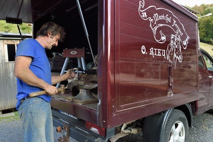 France, Ardèche (07), parc naturel régional des Monts d'Ardèche, massif du Mézenc, Lac-d'Issarlès, Ferme de La Louvèche, le maréchal Ferrant Olivier Rieu travaille un fer à cheval dans son atelier itinérant