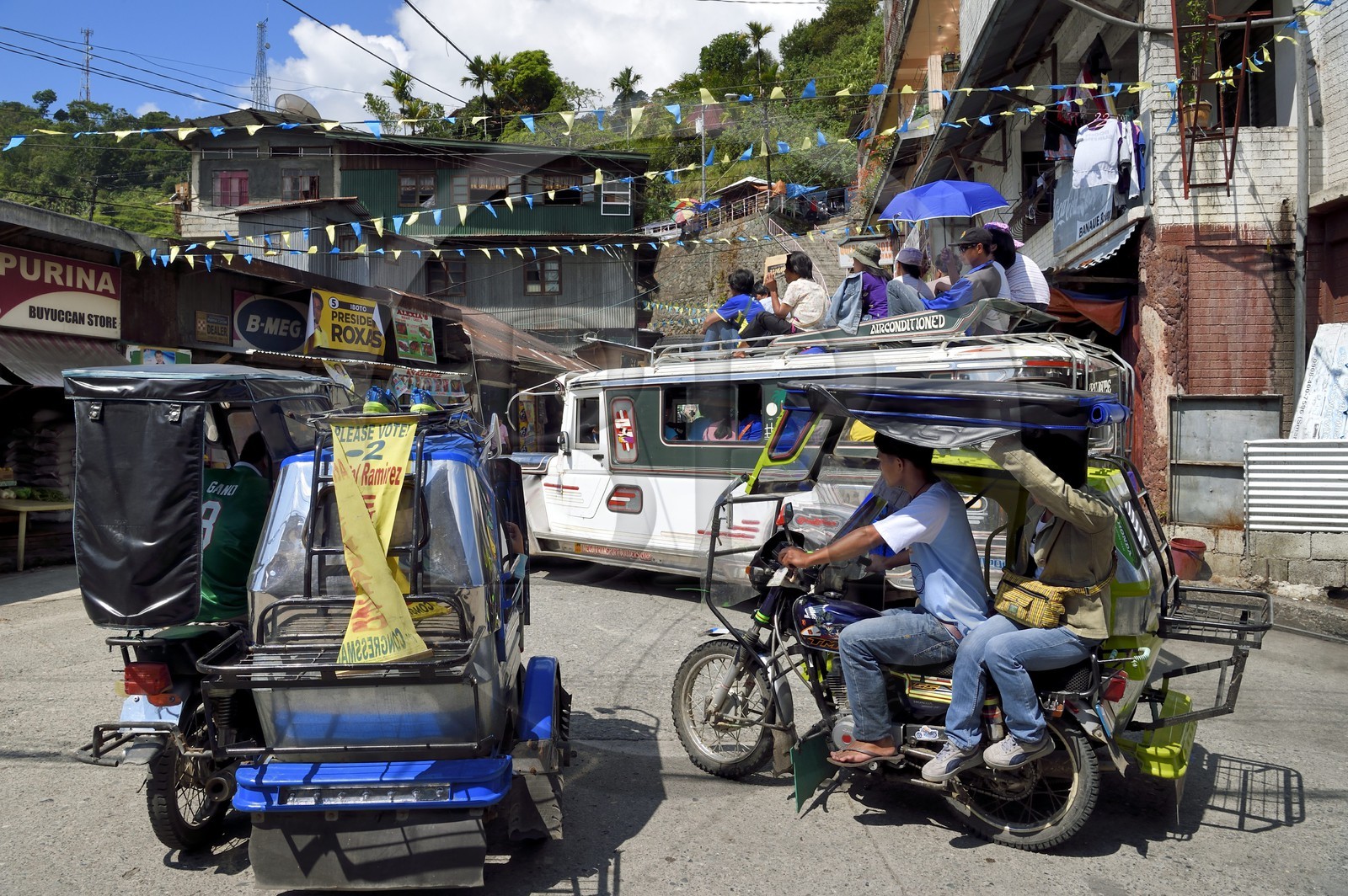 Philippines, Ifugao province, Banaue town, jeepney (elongated jeep to transport passengers) and tricycle motorcycle taxi on the main square, passengers on the roof