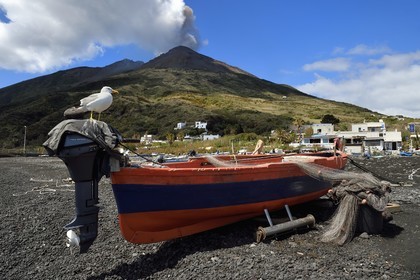 Italie, Sicile, iles Eoliennes, classées Patrimoine Mondial de l'UNESCO, ile de Stromboli, une des multiples et régiulières éruptions du volcan Stromboli qui culmine à 924m, bateau de pêche sur la plage de Scari au premier plan