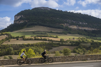 France, Aveyron (12), parc naturel régional des Grands-Causses, Roquefort-sur-Soulzon, cyclistes effectuant l'itinéraire cyclo touristique Brebis'Cyclette en Pays de Roquefort, le rocher du Combalou abritant les fleurines des caves de Roquefort en arrière plan