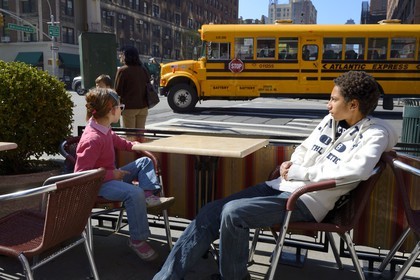 Etats-Unis, New York, Manhattan, Upper West Side, bus scolaire passant devant la terrasse de café à l'angle de Amsterdam Avenue et 79th Street