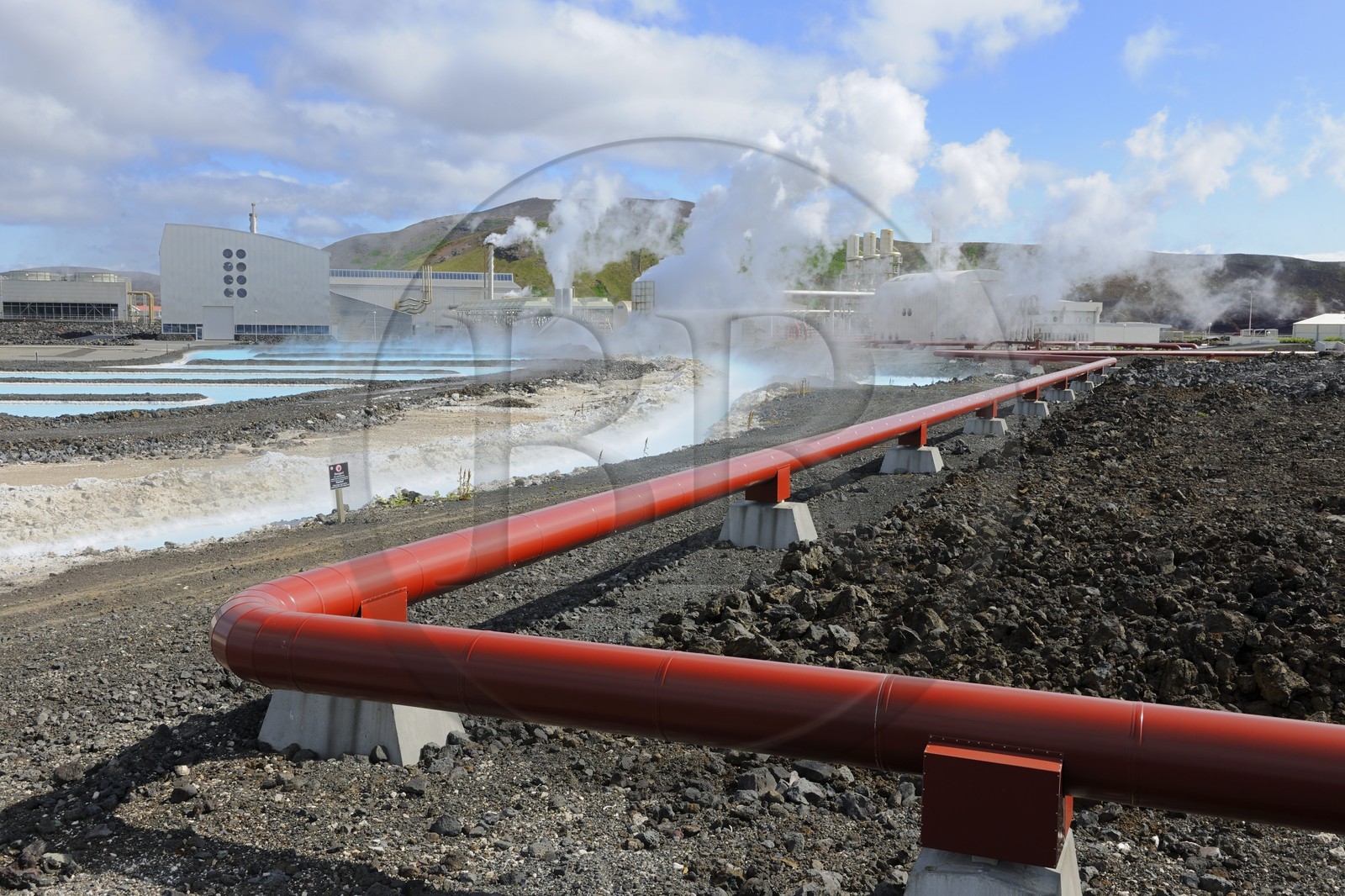 Iceland, Sudurnes Region, Grindavik, the Blue Lagoon with drains and lava in the foreground and the geothermical factory in the background