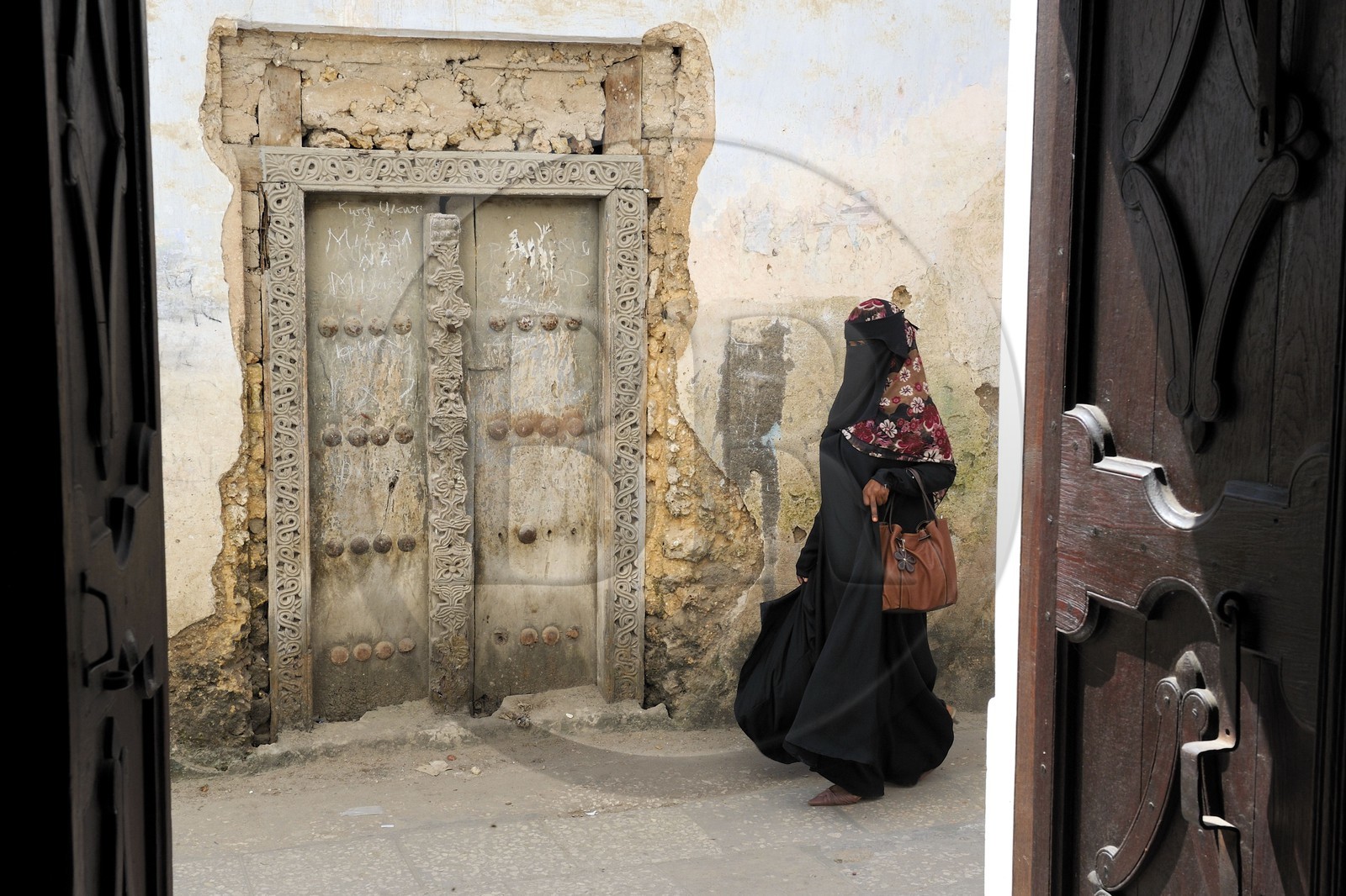 Tanzania, Zanzibar Archipelago, Unguja island (Zanzibar), Stone Town, listed as World Heritage by UNESCO, veiled woman passing by an arabic type door from the old city in the Shangani neighborhood