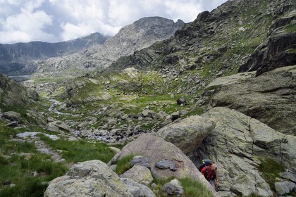 France, Alpes-Maritimes (06), parc national du Mercantour, randonneur passant un seuil sur le sentier de randonnée GR 52, la Vallée des Merveilles parsemée de milliers de gravures rupestres de l'Age de bronze et la Paroi vitrifiée en arrière plan