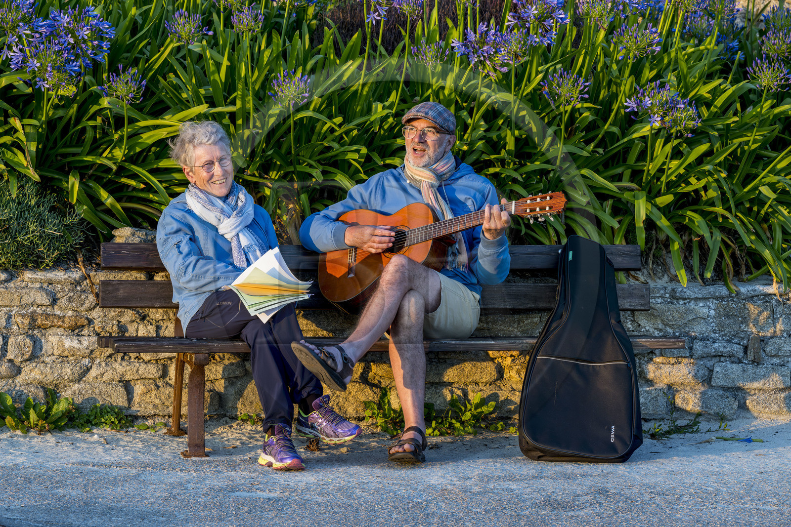 France, Finistère, Ponant Islands, Ile de Batz (Batz Island), Remi plays guitar for Françoise on a bench at the pier at the end of the day