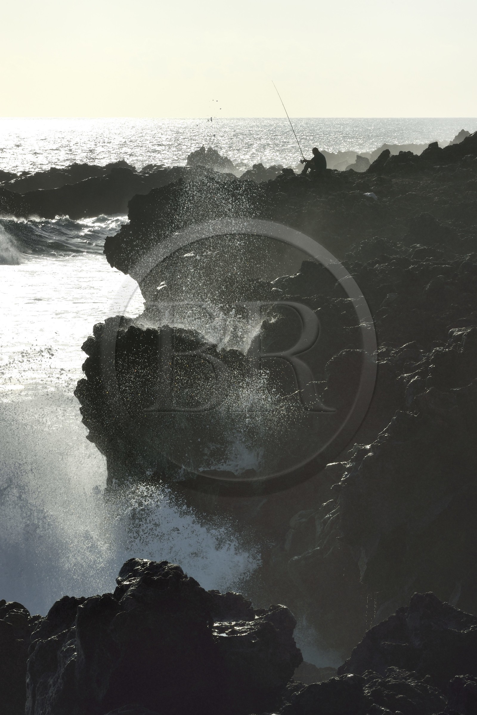 France, Ile de la Reunion, L'Etang Salé les Bains, la côte entre Le Gouffre et l'Etang du Gol, roches noires basaltiques d'origine volcanique tourmentées par l'océan, pêcheur à la ligne