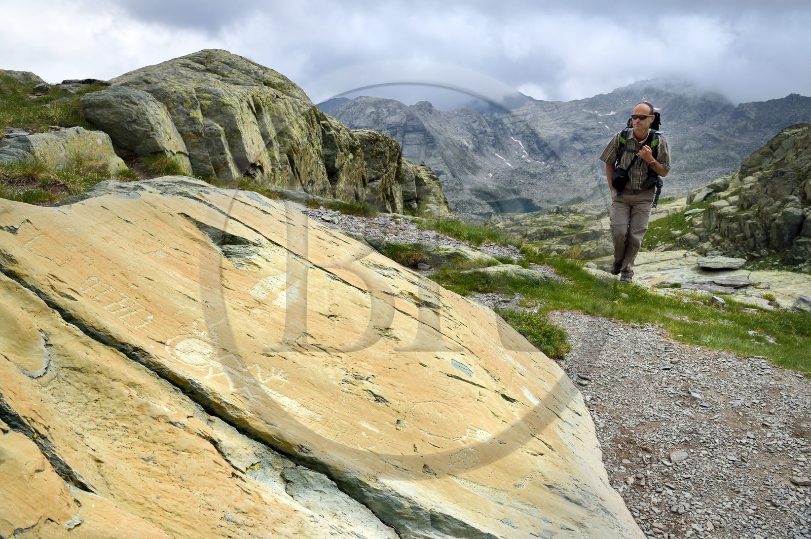 France, Alpes-Maritimes (06), parc national du Mercantour, Vallée des Merveilles parsemée de milliers de gravures rupestres de l'Age de bronze, Pas de l'Arpette, randonneur approchant la gravure baptisée l'Anthropomorphe aux bras en zigzag, un réticulé de cases qui symboliserait les champs cultivés à gauche et deux poignards