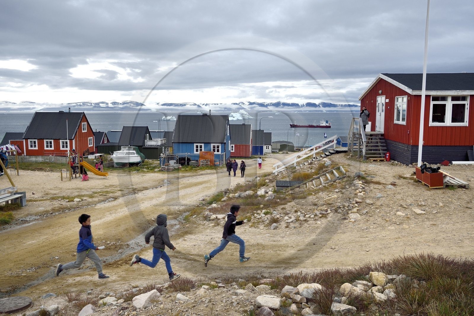 Greenland, North West coast, Baffin Sea, Qaanaaq or New Thule, Inuit children run to join their schoolmistress, an iceberg in the background