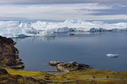 Greenland, west coast, Disko Bay, Ilulissat, icefjord listed as World heritage by UNESCO that is the mouth of the Sermeq Kujalleq Glacier (Jakobshavn Glacier), hiking on the wooden walkway going to the Sermermiut site and fishing boat at the foot of icebergs
