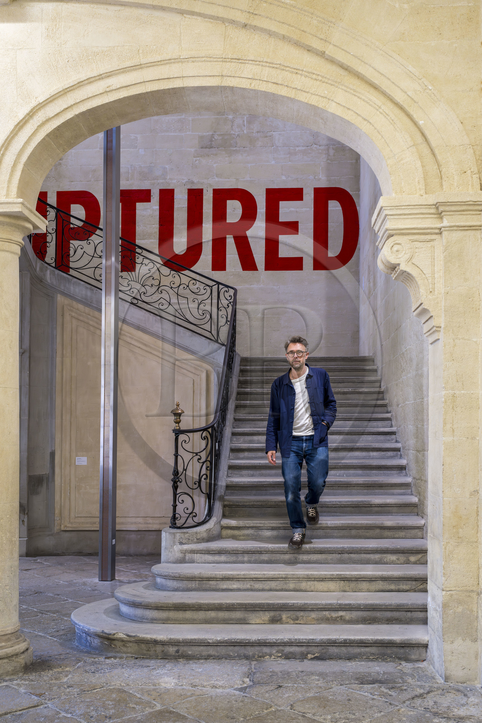 France, Vaucluse (84), Avignon, Collection Lambert, Musée d'Art Contemporain, aménagé dans les hôtels particuliers de Caumont et de Montfaucon du XVIIIe siècle, Stéphane Ibars, directeur artistique de la Collection descend l'escalier sous Ruptured (1970) de l'artiste Lawrence Weiner