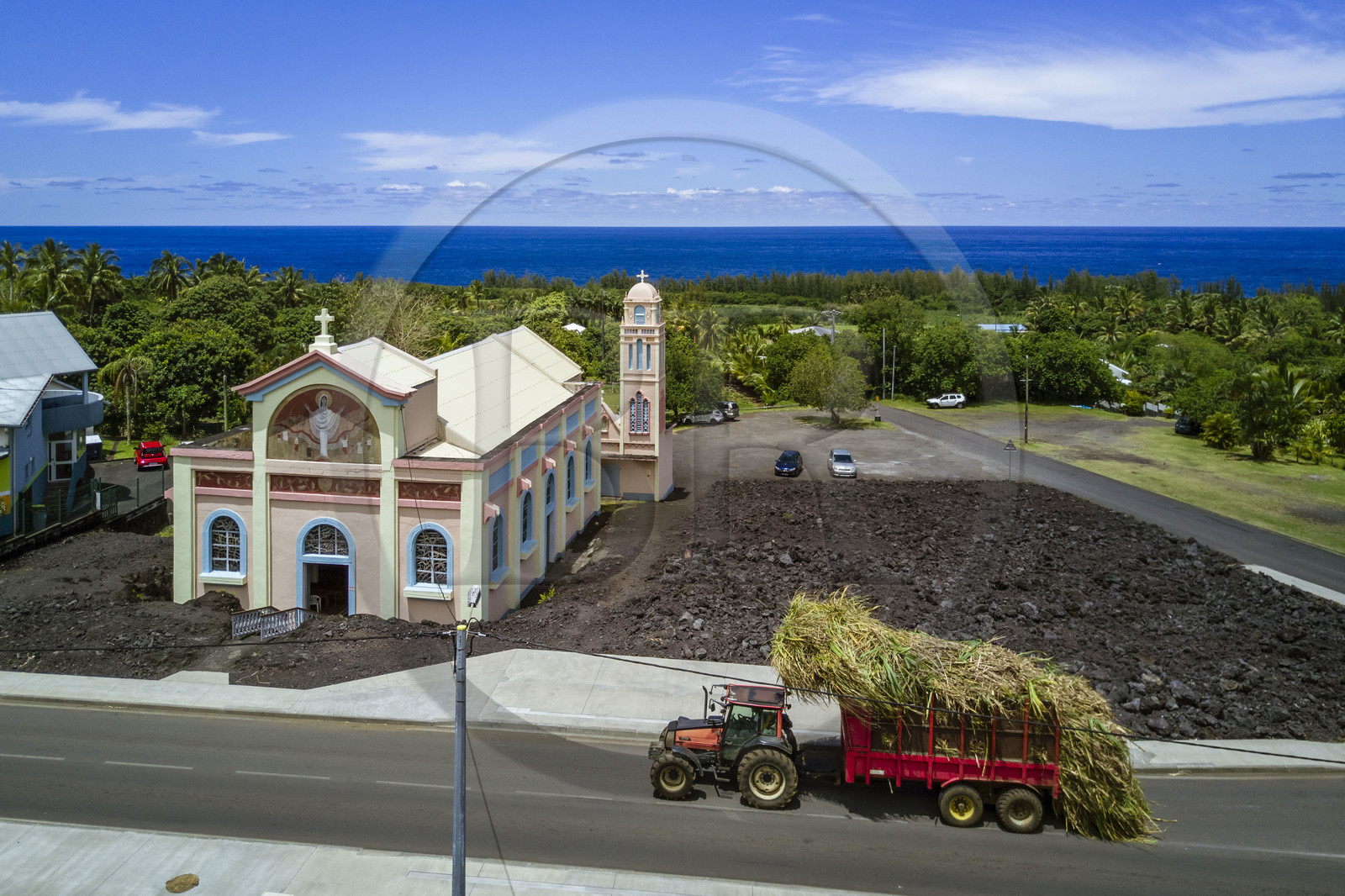 France, Reunion island (French overseas department), the Notre-Dame-des-Laves church of Piton Sainte-Rose spared by the lava flow of 1977, tractor carrying a load of sugar cane to sugar factory (aerial view)