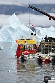 Greenland, west coast, Uummannaq, fishing boat unloading in port and icebergs in the background