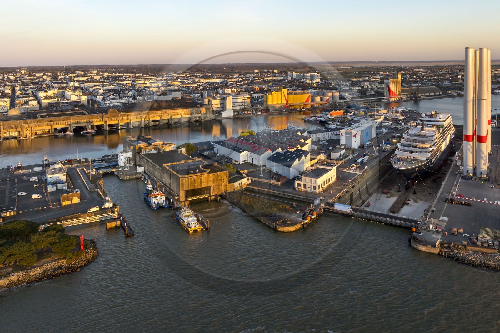 France, Loire Atlantique, Saint Nazaire, the former German submarine base built during the last world war border the dock of the harbour basin of Saint-Nazaire, the East lock and the fortified lock in the foreground and the construction site of the luxury super-yacht Ritz-Carlton Luminara in the Joubert dry dock on the right, the wind turbine towers are stored before embarkation (aerial view)