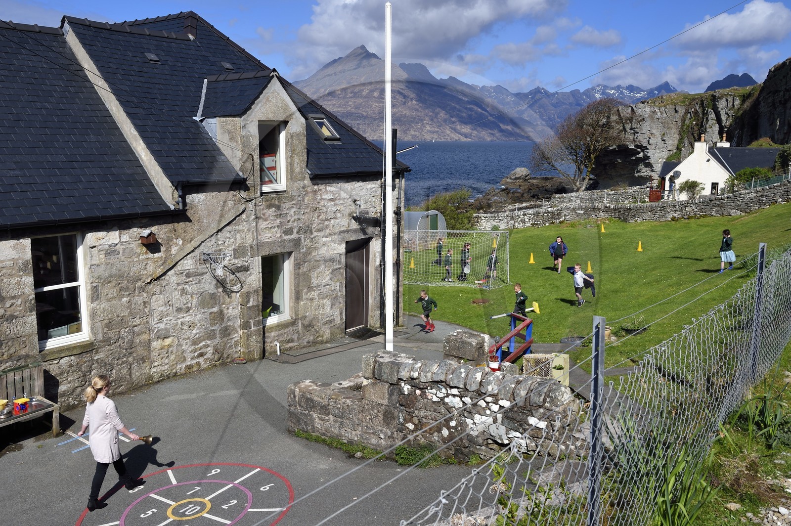 Royaume-Uni, Ecosse, région des Highlands, les Hébrides, Ile de Skye, village de Elgol sur les rives du Loch Scavaig au bout de la péninsule de Strathaird et le massif des Black Cuillin Mountains en arrière plan, enfants jouant au rounders dans le jardin de l'école