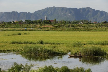 Vietnam, province de Ninh Binh, pêcheur en barque devant un village chrétien