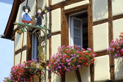 France, Haut-Rhin (68), Eguisheim, labellisé Les Plus Beaux Villages de France, enseigne de boulangerie avec des personnages en costume alsacien devant une maison à colombage