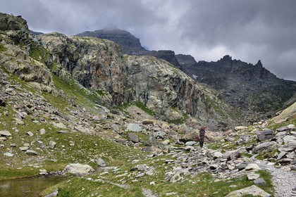 France, Alpes-Maritimes, parc national du Mercantour (Mercantour National Park), the Vallee des Merveilles (Valley of Wonders) scattered with thousands of rupestral engravings of the Bronze Age, hiker on the trail GR 52 at the Merveilles Lake below the Baisse (pass) de Valmasque and the Mont Grand Capelet (2915 m) in the background left