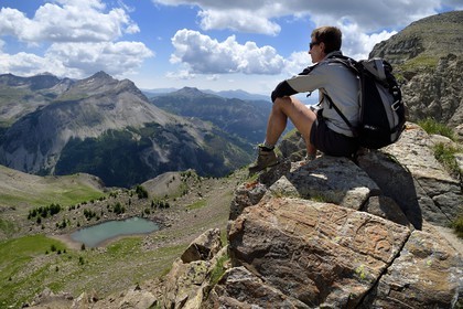 France, Alpes de Haute Provence, Uvernet Fours, Mercantour National Park, Ubaye valley, lake tour hiking trail of the Cayolle pass at the Pas du Lausson, François Breton park guard sitting on a boundary engraved on rocks delimiting the border between the Duchy of Savoy and the County of Nice, Haut-Var Valley and Lake Lausson (Alpes-Maritimes) in the background