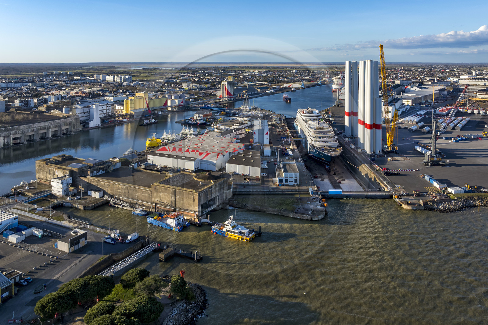 France, Loire Atlantique, Saint Nazaire, the East lock and the fortified lock of the former German submarine base built during the last world war in the foreground and the construction site of the luxury super-yacht Ritz-Carlton Luminara in the Joubert dry dock, the wind turbine towers on the right are stored before embarkation (aerial view)