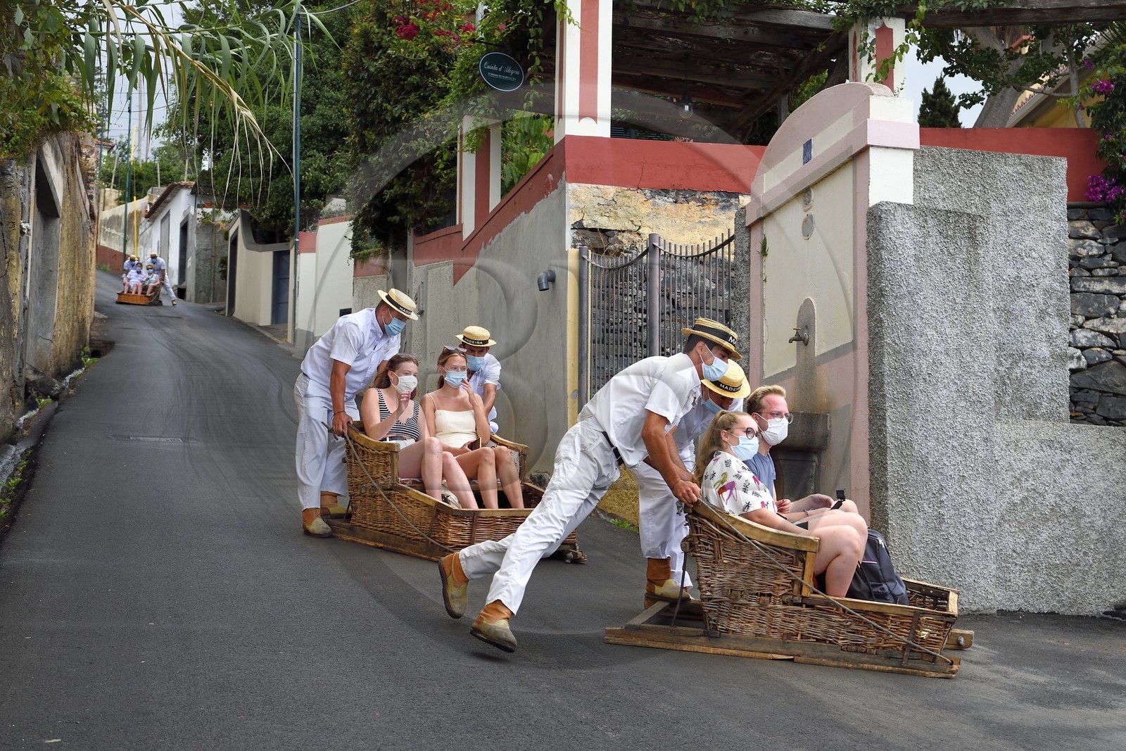 Portugal, Madeira Island, Funchal, tourists descending from the tropical garden in traditional wicker basket on the road camino do Monte